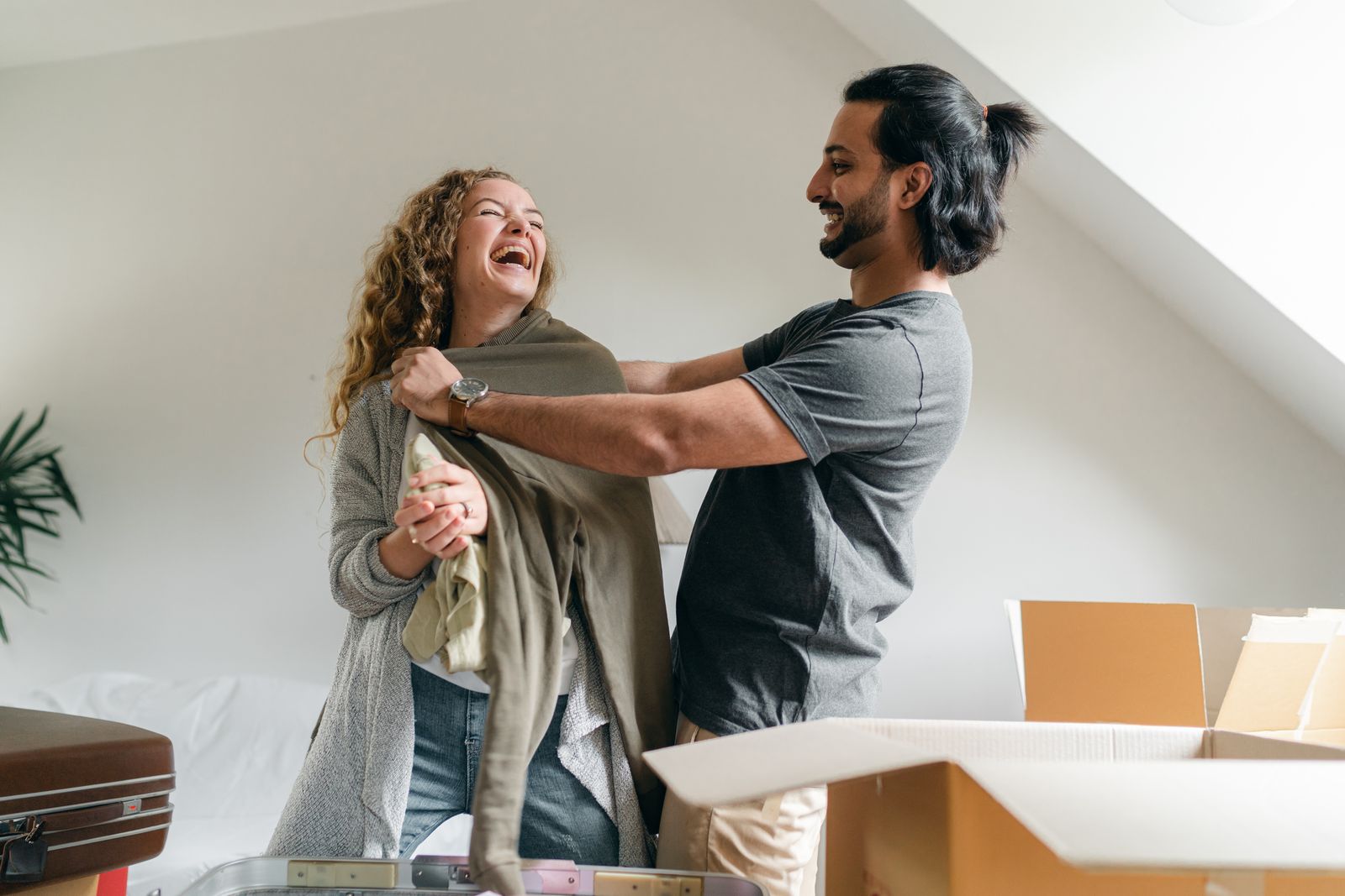Two adults laughing beside moving boxes while unpacking in a home